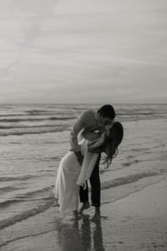 a man and woman kissing on the beach by the water's edge in black and white