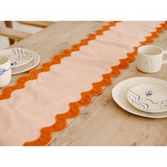 an orange and white table runner on top of a wooden table with plates, cups and saucers