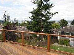 a wooden deck with railings and trees in the back yard, overlooking houses on a cloudy day