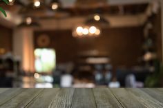 an empty wooden table top in front of a blurry room with lights hanging from the ceiling