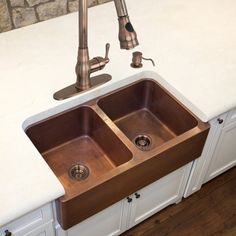 a kitchen sink with two copper faucets and a white counter top in front of a brick wall