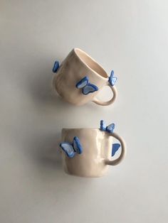 two coffee mugs with blue butterflies on them sitting next to each other in front of a white background