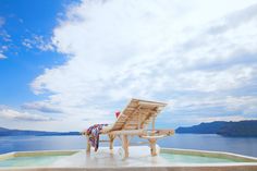 a wooden chair sitting on top of a cement platform next to the ocean under a cloudy blue sky