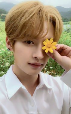 a young man holding a yellow flower in front of his face