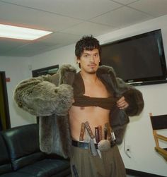 a man with no shirt on standing in front of a tv and holding his jacket over his chest