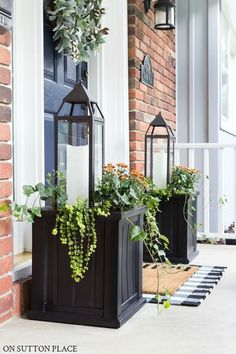 two planters with plants are on the front porch and one has a candle holder