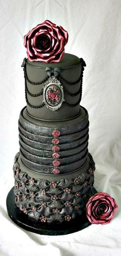 a black and red wedding cake with roses on it's tiers, sitting on a white background