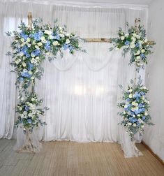 an arch decorated with flowers and greenery in front of a white drape curtain