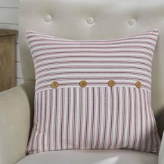 a red and white striped pillow with gold buttons on it sitting in a beige chair