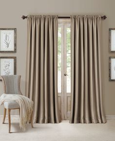 a living room with beige curtains and pictures on the wall above it, along with a chair