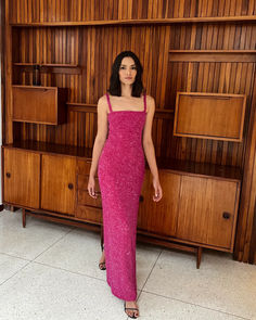 a woman standing in front of a bookcase wearing a pink dress and high heels