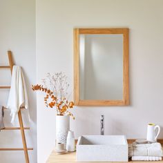 a bathroom sink sitting under a mirror next to a wooden ladder and vase with flowers