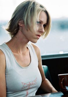 a woman sitting at a table with a coffee cup in her hand and looking off into the distance