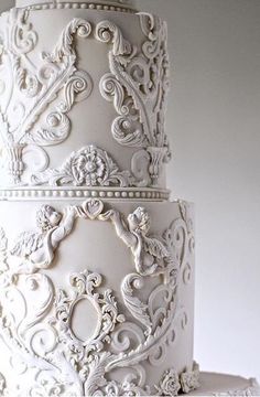 a three tiered white wedding cake with intricate designs