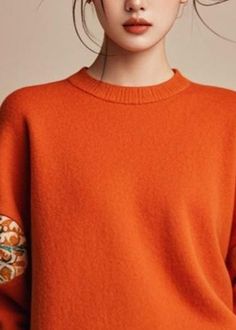 a woman wearing an orange sweater with flowers on the sleeves and arms, looking at the camera