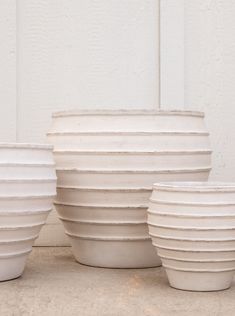 several white vases sitting next to each other in front of a wall with no one around them