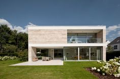 a modern house with an open patio and lawn area in the foreground, surrounded by white flowers