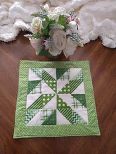 a green and white quilted table runner next to a vase with flowers on it