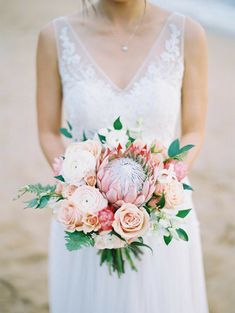 a bride holding a bouquet of flowers on the beach