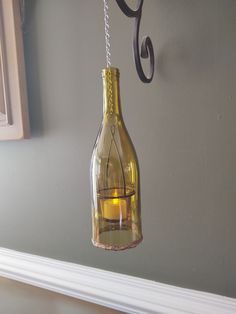 a wine bottle hanging from a hook on the wall next to a candle holder with a lit candle in it