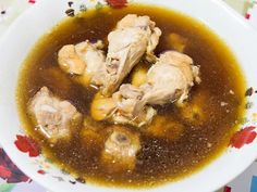 a white bowl filled with soup and meat on top of a floral tablecloth covered table