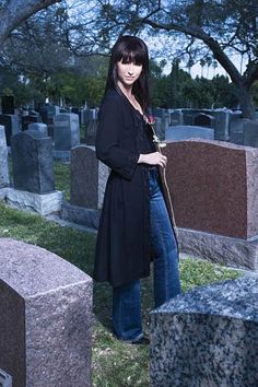 a woman standing in the middle of a cemetery with her hands on her hips and looking at the camera