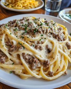 a plate of pasta with meat and cheese on it sitting on a table next to glasses