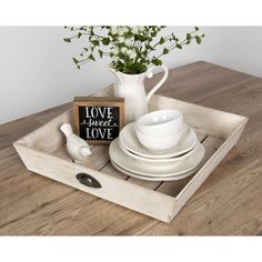 a wooden tray with white dishes and flowers in it