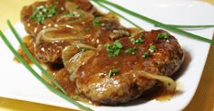 some meat and onions on a white plate with green onion garnishes in gravy