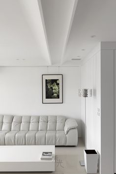 a white living room with a couch and coffee table in the center, along with a painting on the wall