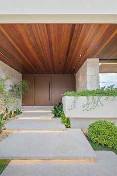 the entrance to a modern house with wood and stone walls, concrete steps and plants on either side