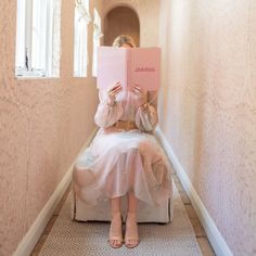 a woman sitting in a chair reading a pink book with her hands on her face