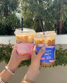 two people holding up drinks in plastic cups with straws on top and palm trees behind them