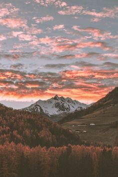 the mountains are covered in trees and clouds as the sun is setting over them,