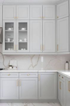 a kitchen with white cabinets and marble counter tops, gold trim on the door handles