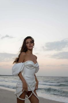 a woman standing on top of a sandy beach next to the ocean wearing a white dress