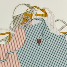 five aprons are lined up in different colors and sizes, one has a wooden spoon sticking out of it