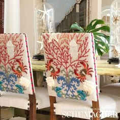 two chairs with embroidered designs on them sit in front of a dining room table and mirror