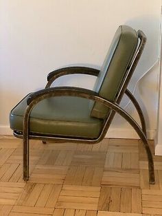 a green leather chair sitting on top of a hard wood floor next to a white wall