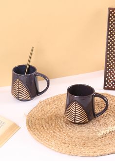 two coffee mugs sitting on top of a placemat next to an open book