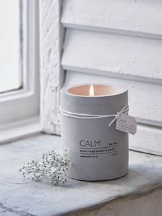 a candle that is sitting on a window sill next to some flowers and a tag