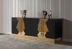 a black and gold sideboard with two golden sculptures on it's sides, in front of a striped wall