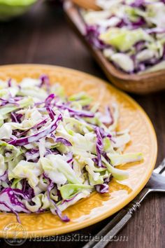 a plate with coleslaw on it next to a fork and bowl full of coleslaw