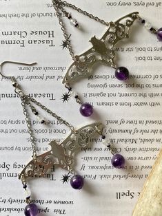 Cast bat charms drop from stainless steel chain with Czech glass beads, flashy faceted Moonstone, and deep dreamy Amethyst--a combination of stones which will keep you calm and collected amidst any chaos! Connecting to the divine energy of the moon, Moonstone enhances intuition and psychic energy. Working through the heart, third eye and crown chakras, it allows you to see past the obvious to deep and hidden truths. Just as the moon waxes and wanes, moonstone can help in processing changed and b Mystical Dangle Jewelry For Halloween, Purple Pierced Metal Jewelry, Purple Metal Pierced Jewelry, Witchy Dangle Metal Jewelry, Witchy Metal Dangle Jewelry, Mystical Nickel-free Purple Jewelry, Mystical Purple Nickel-free Jewelry, Purple Crystal Metal Earrings For Gifts, Purple Metal Crystal Earrings As Gift