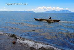 a man in a small boat on the water with mountains in the background and blue sky