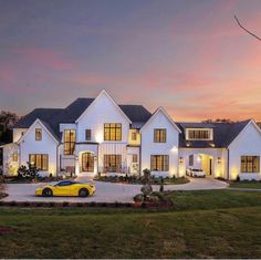 a yellow sports car parked in front of a large white house at dusk with lights on