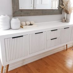 a white dresser with two vases on top and a mirror above it in a room