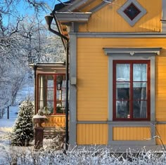 a yellow house with red windows and snow on the ground