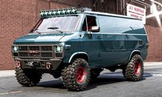 a green truck with red wheels parked in front of a brick building on the street