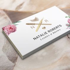 a business card with pink roses and gold scissors on it, sitting on a marble surface